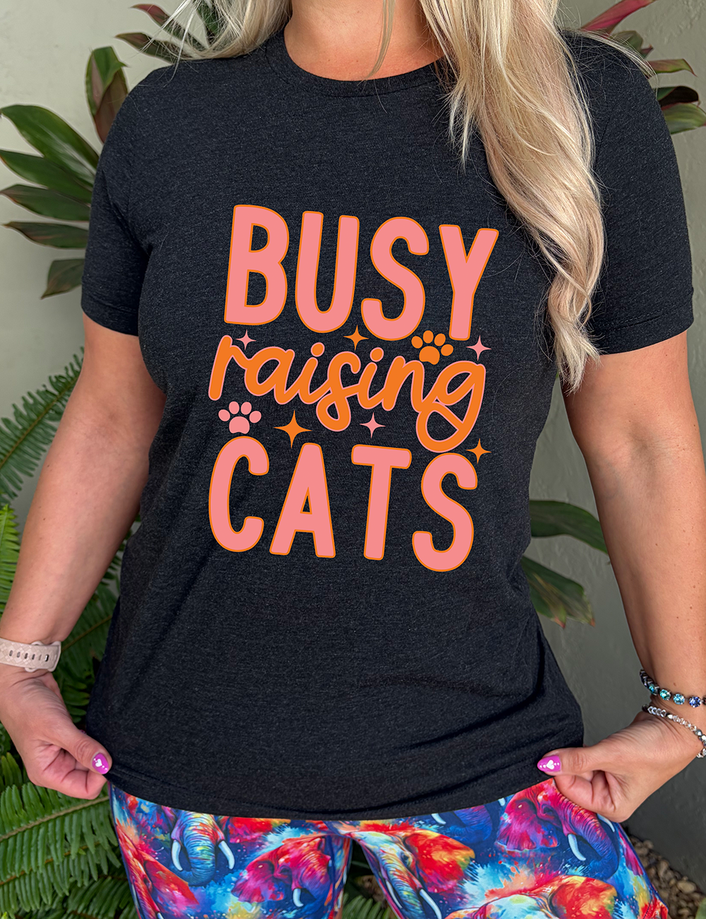 black unisex tee with the words "busy raising cats" on it, with graphics of a couple small paw prints and a number of little stars