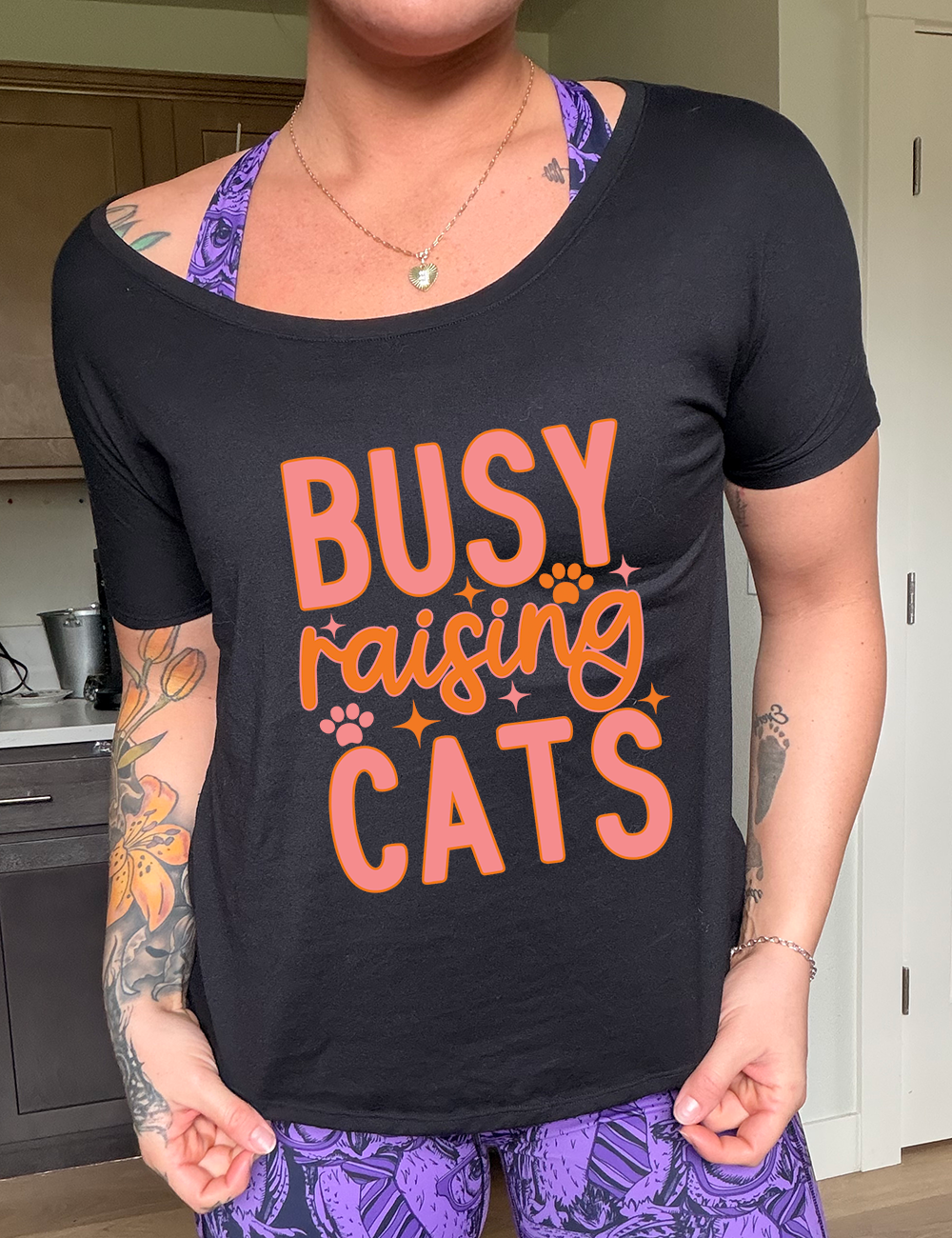black slouchy tee with the words "busy raising cats" on it, with graphics of a couple small paw prints and a number of little stars