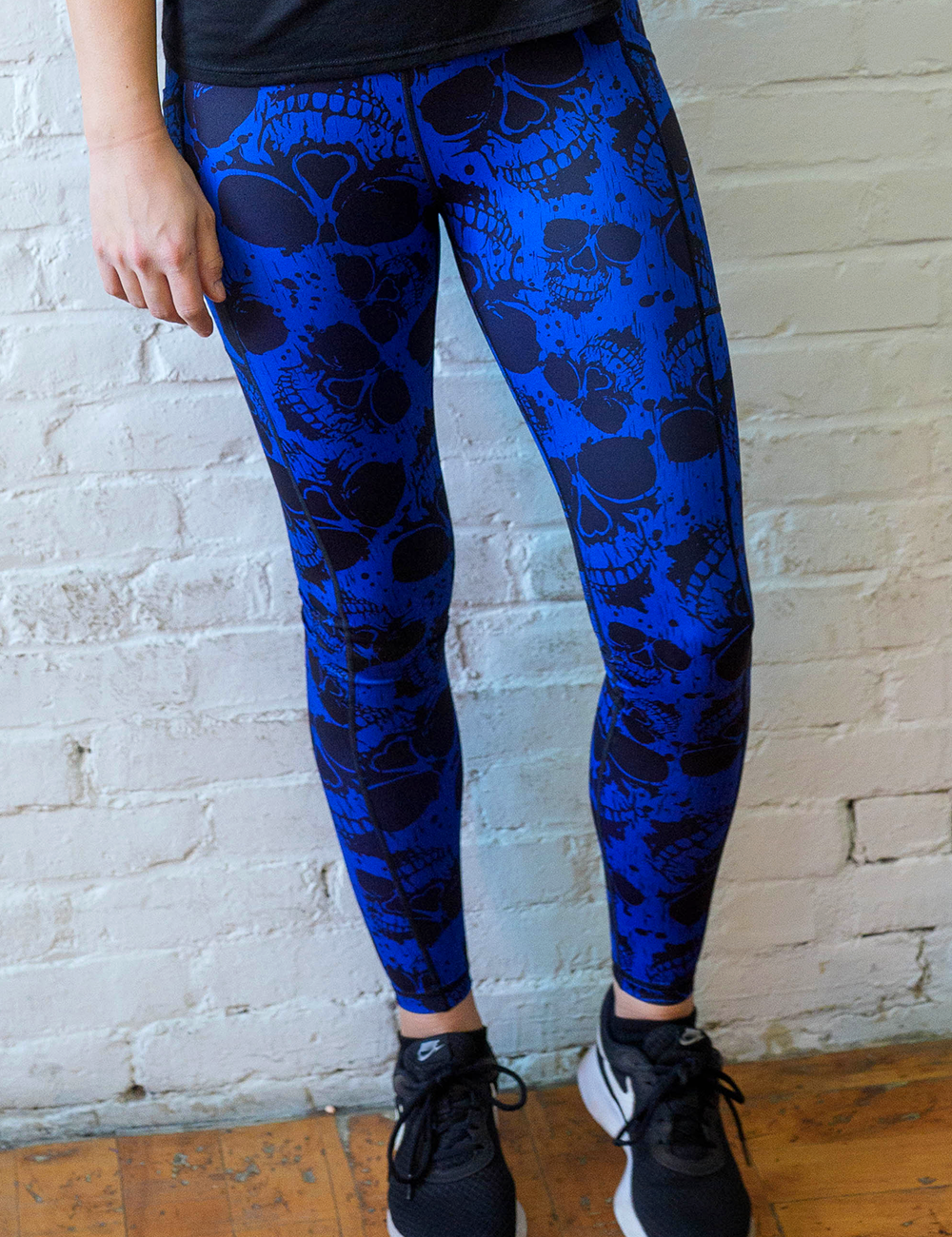 model wearing the dark skulls against a blue background pattern full length leggings in front of a white brick wall