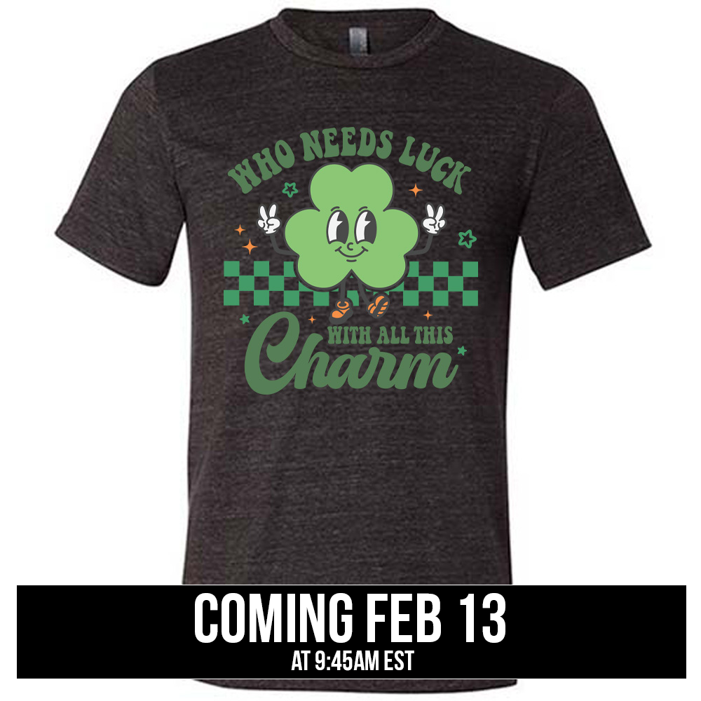black unisex tee with the words "who needs luck with all this charm" on it, with the graphic of a cheerful shamrock (with eyes, nose and smiling mouth) giving two peace signs with its hands, in front of a partial checkered background, with a few stars around, coming soon