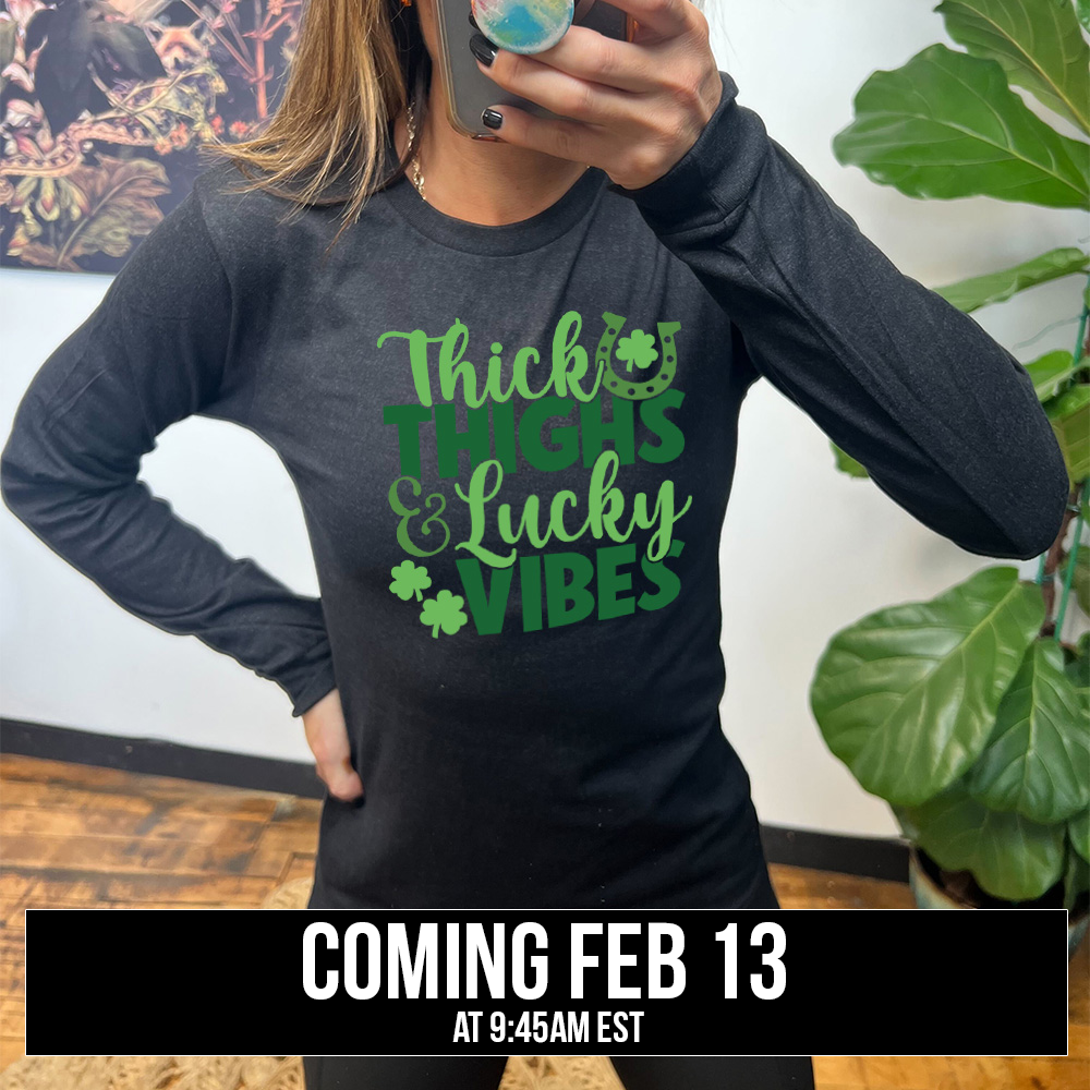 heather black long sleeve with the words "thick thighs & lucky vibes" on it, with graphics of a horseshoe and a few shamrocks, coming soon