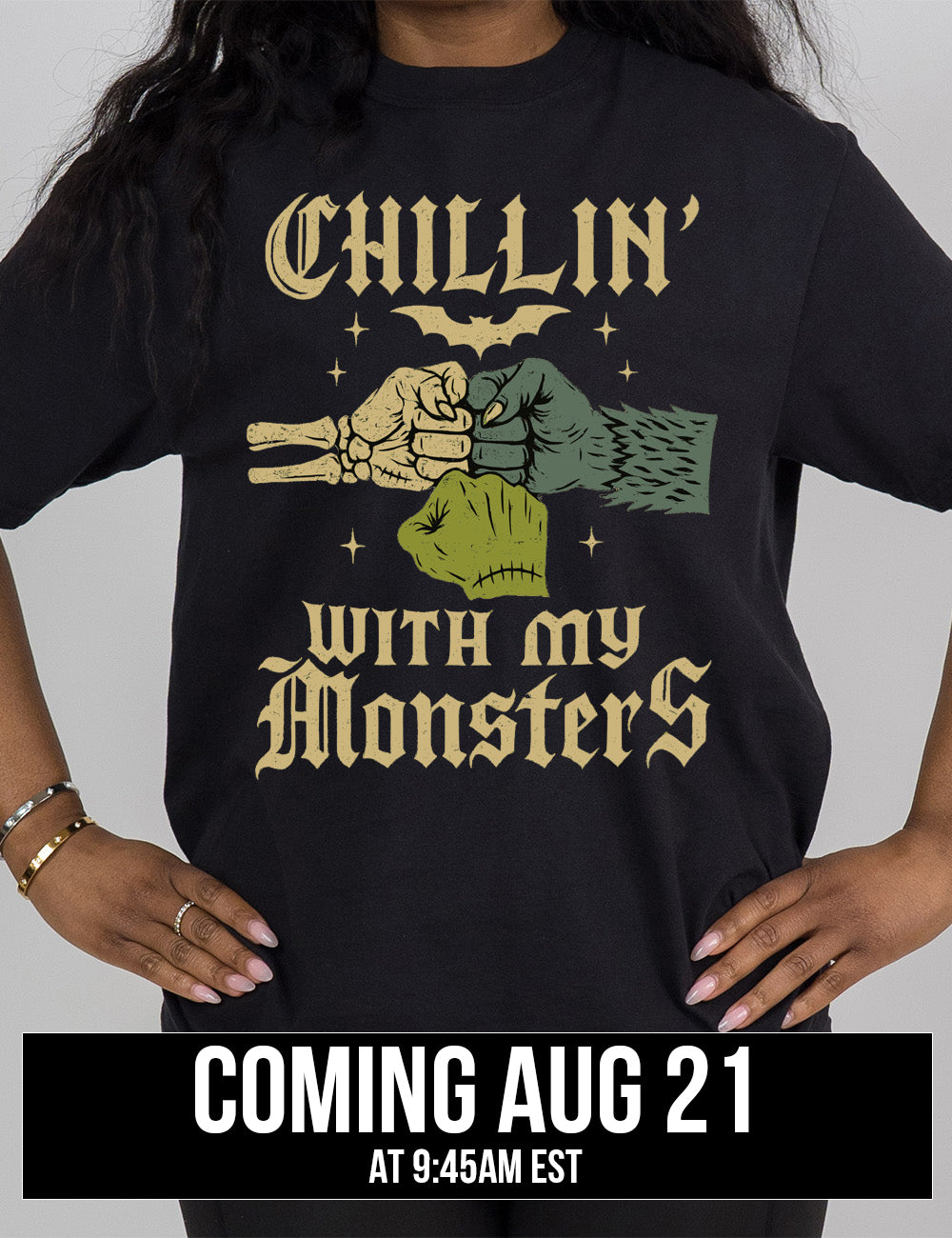 black modern tee with the words "chillin' with my monsters" around the graphic of a skeleton's hand, a werewolf's hand, and a zombie's hand, doing a fist pump, with a bat above, and few stars around, coming august 21st