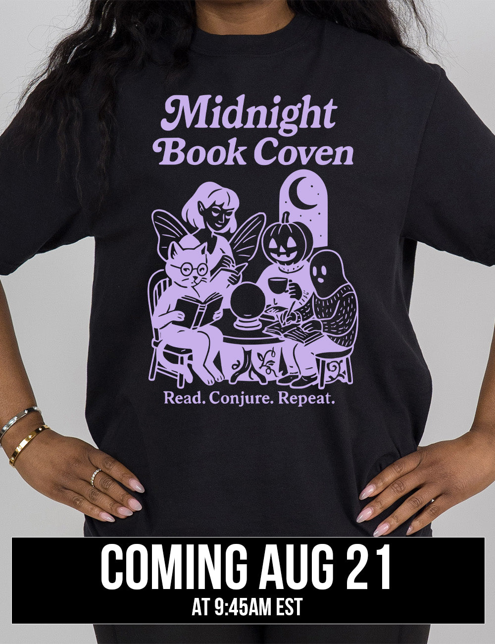 black modern tee with words "midnight book coven" above the graphic of a tombstone with a moon on it, a fairy reading a book, a pumpkin head person drinking coffee with a book, a ghost wearing a sweater and writing in a journal, and a humanoid cat wearing glasses, giving side-eye, and reading a book, all around a table with a crystal ball on top, and the words underneath saying "read. conjure. repeat." coming august 21st