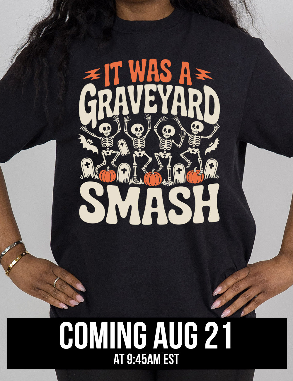 black modern tee with the words "it was a graveyard smash" with a lightning bolt on either side of the words "it was a" and the large graphic in the middle of the words of four skeletons dancing next to tombstones, pumpkins, and two bats, coming august 21st