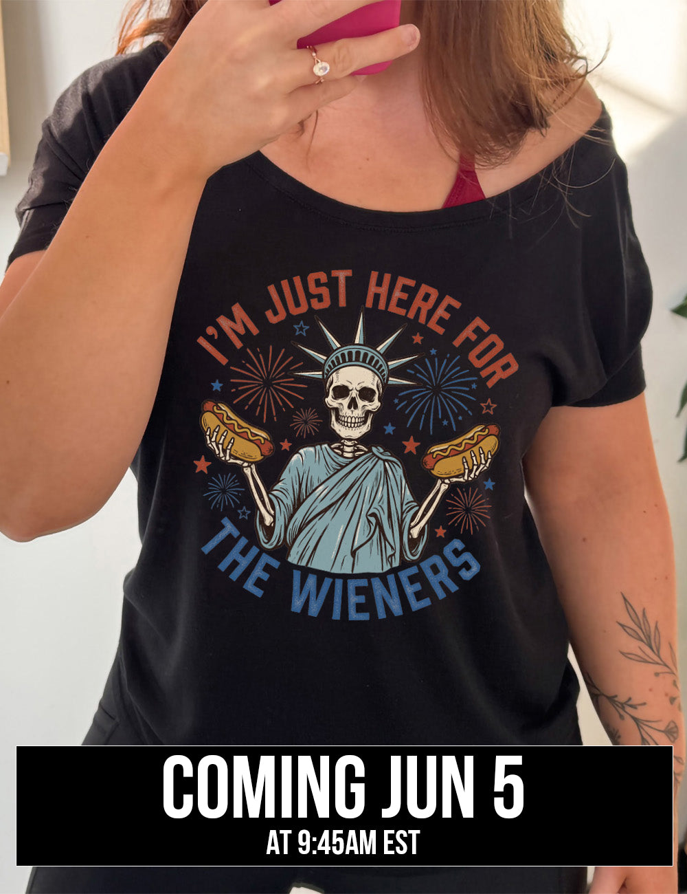 Black slouchy tee with the words "I'm just here for the wieners" on it, with the graphic in the middle of the words of a skeletal statue of liberty with a hotdog in each hand and fireworks and stars around it, coming june 5th