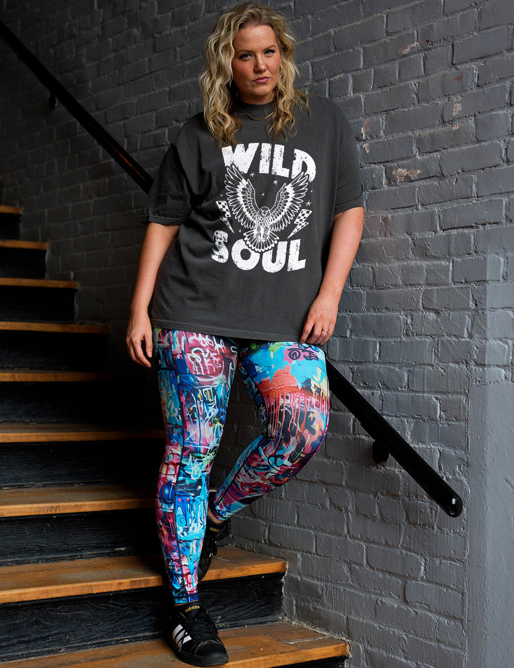 model wearing the full length graffiti pattern leggings posing in the stairwell with a pepper modern tee that reads wild soul with a eagle in the middle