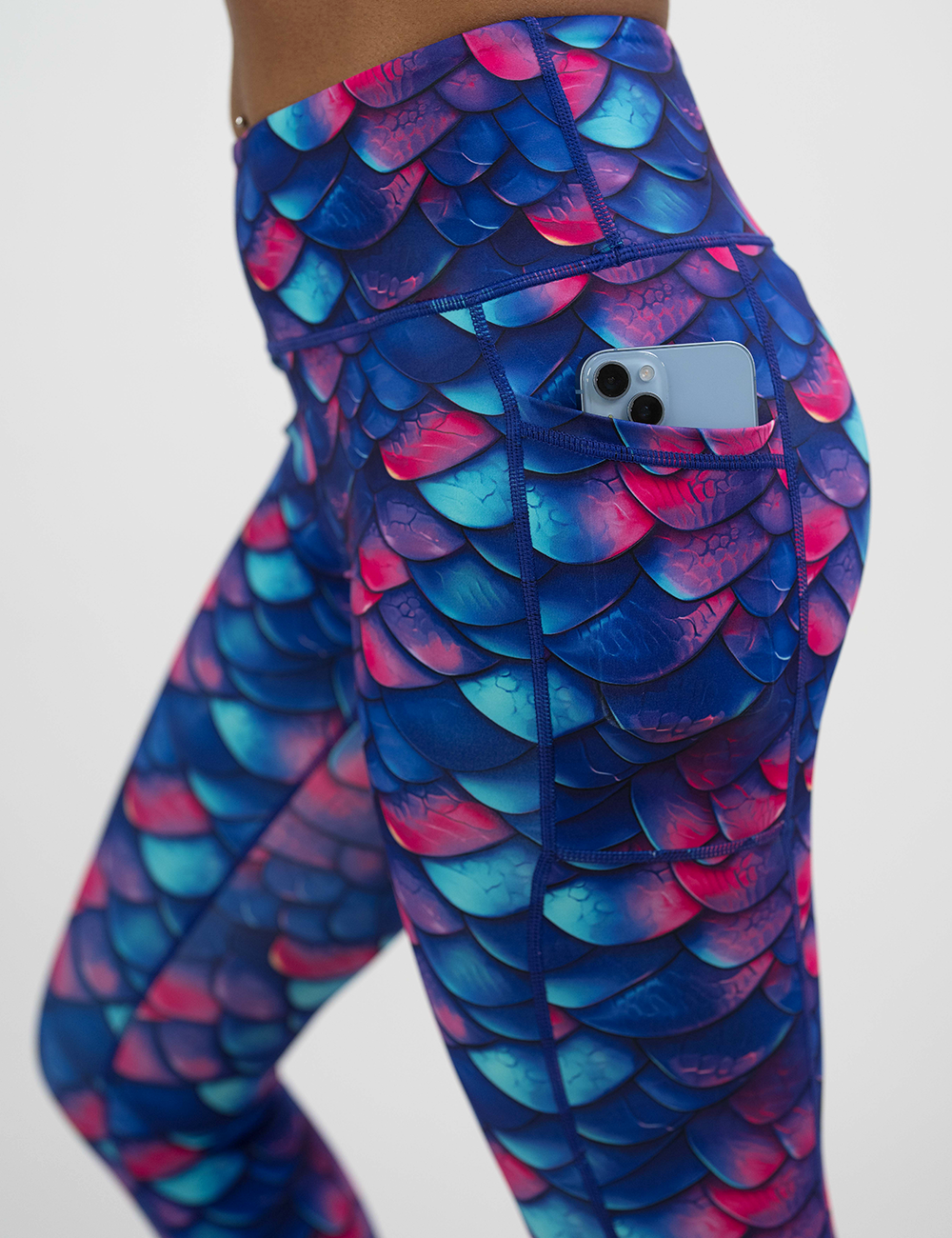 close up of the blue, purple, and red colored dragon scale leggings with a phone in its pocket against a white background