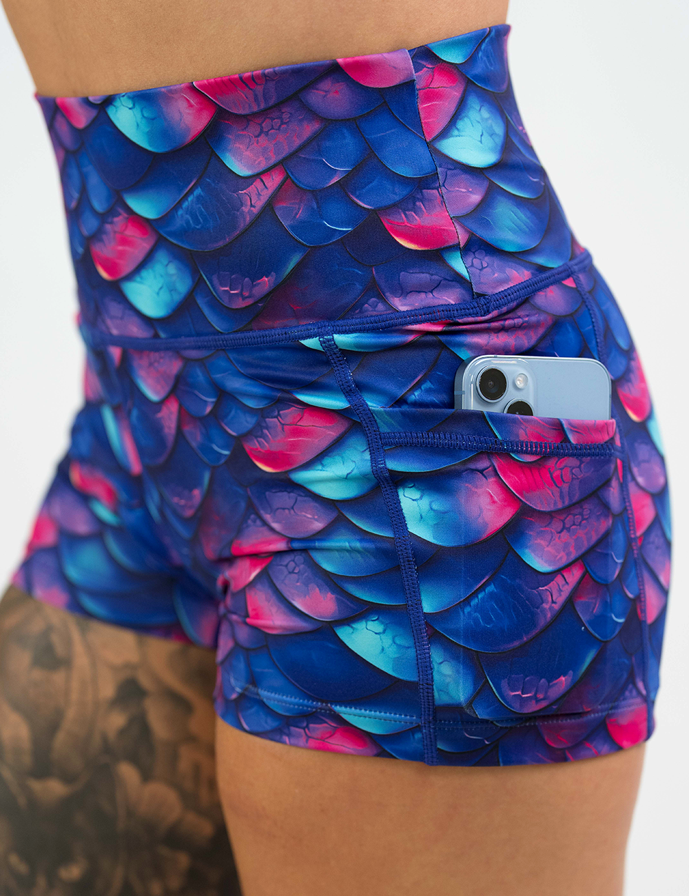close up of the blue, purple, and red colored dragon scale shorts showing the pocket holding a phone