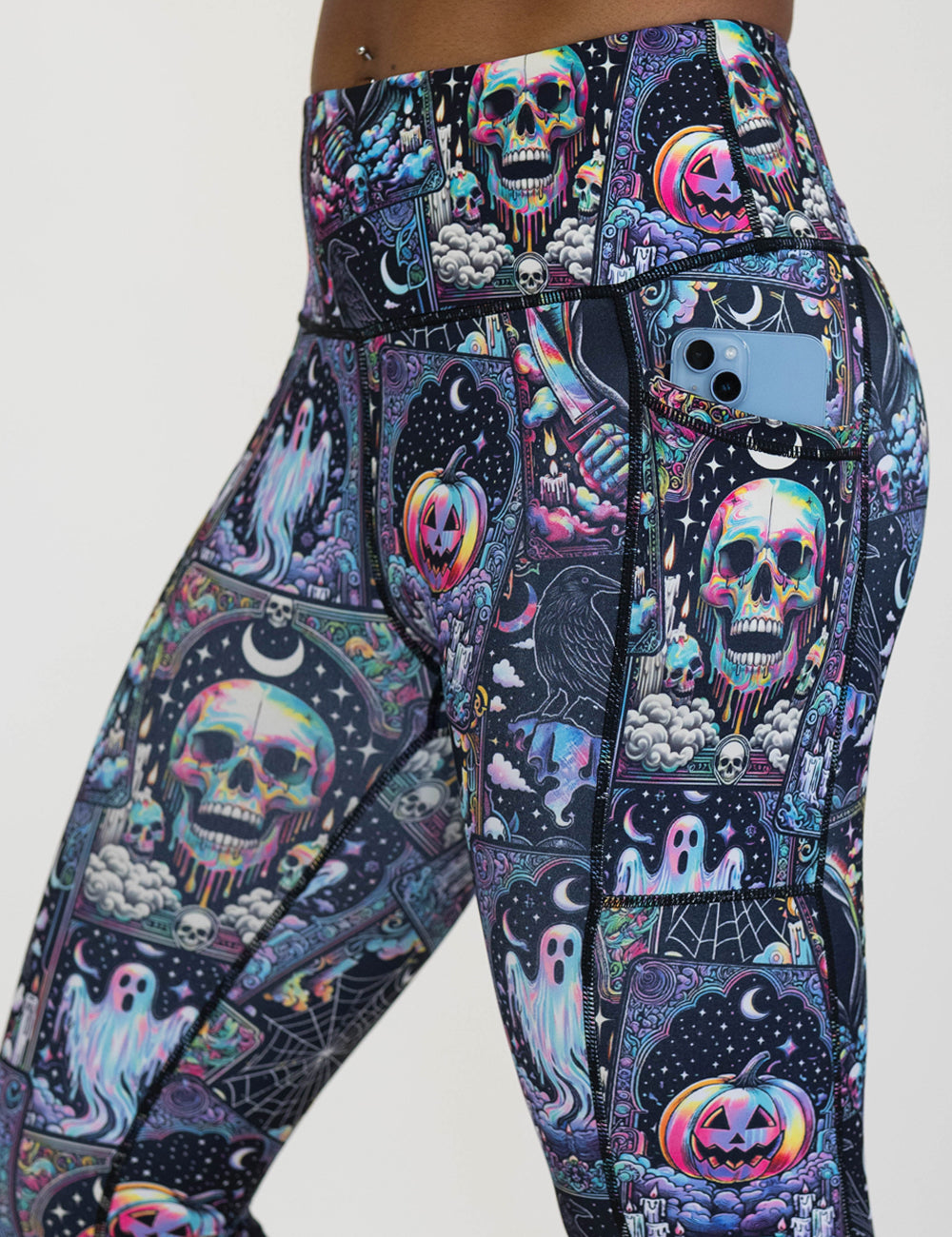 close up of the rainbow skulls, jack o lantern, and ghosts leggings with a phone in its pocket