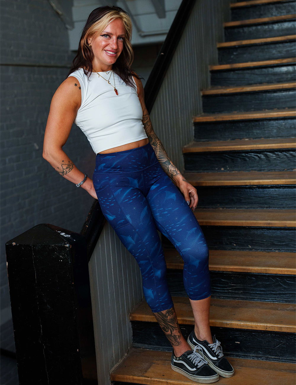 model wearing the capri dark blue ocean filled with sting rays, whales, and fish leggings in a stairwell