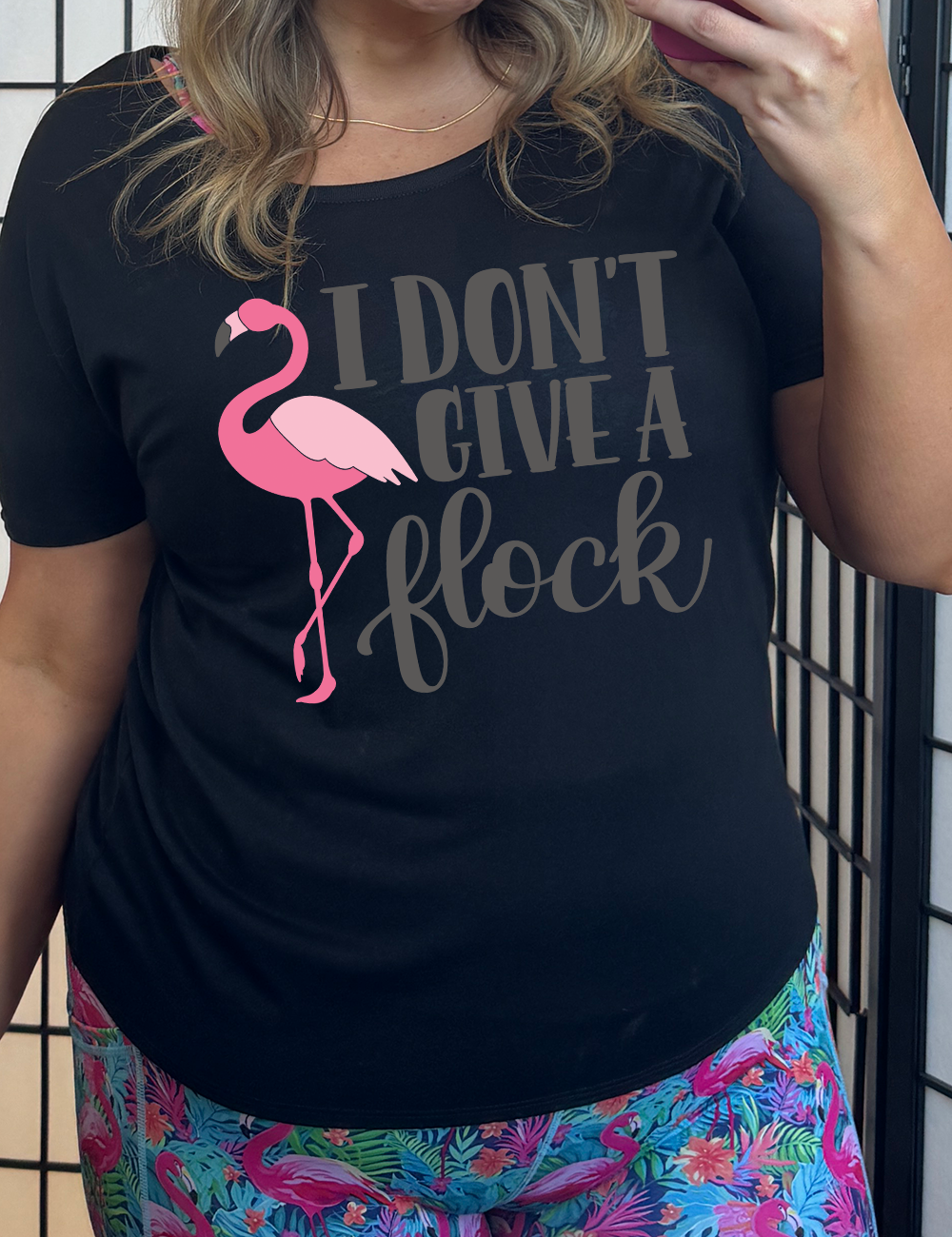 black slouchy tee with the words "I don't give a flock" on it, with the graphic of a flamingo next to these words, leg raised