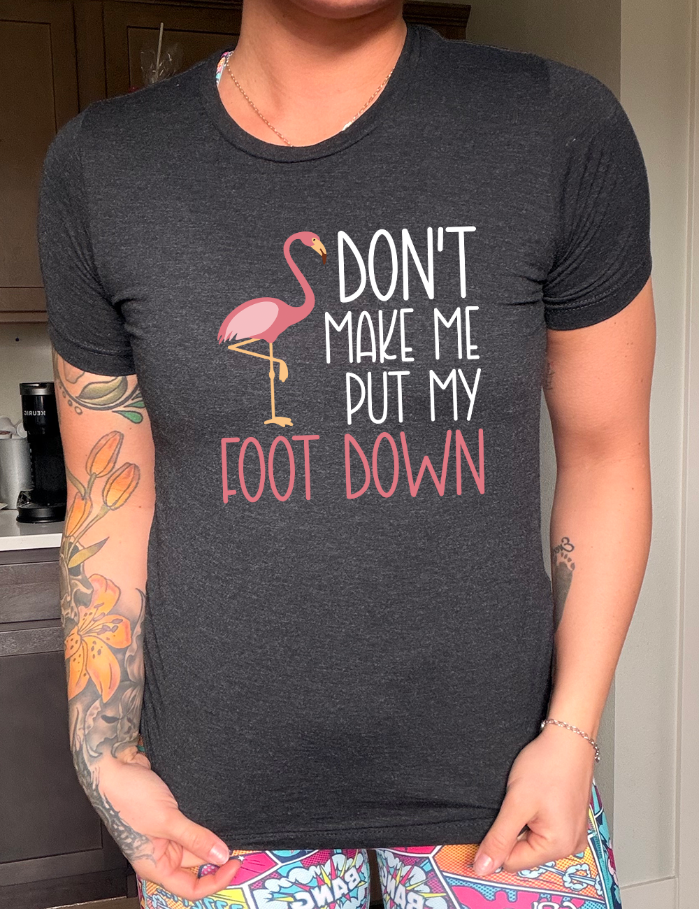 black unisex tee with the words "don't make me put my foot down" on it, with the graphic of a flamingo next to the words, with its foot raised