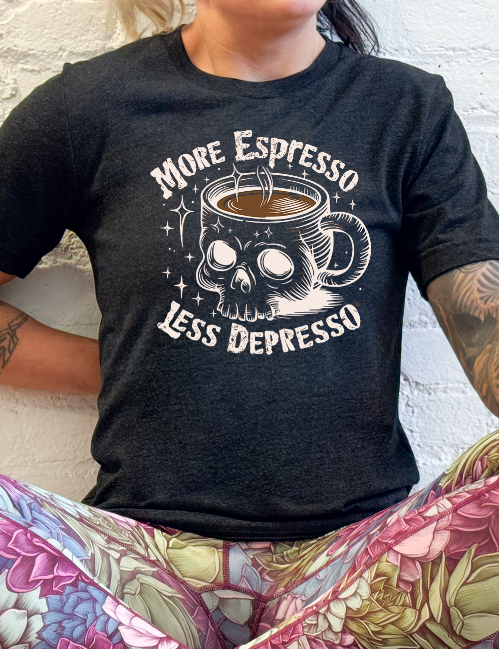 black unisex tee with the words "more espresso less depresso on it, around the graphic of a skull-shaped mug full of a steaming beverage, with lots of little stars around
