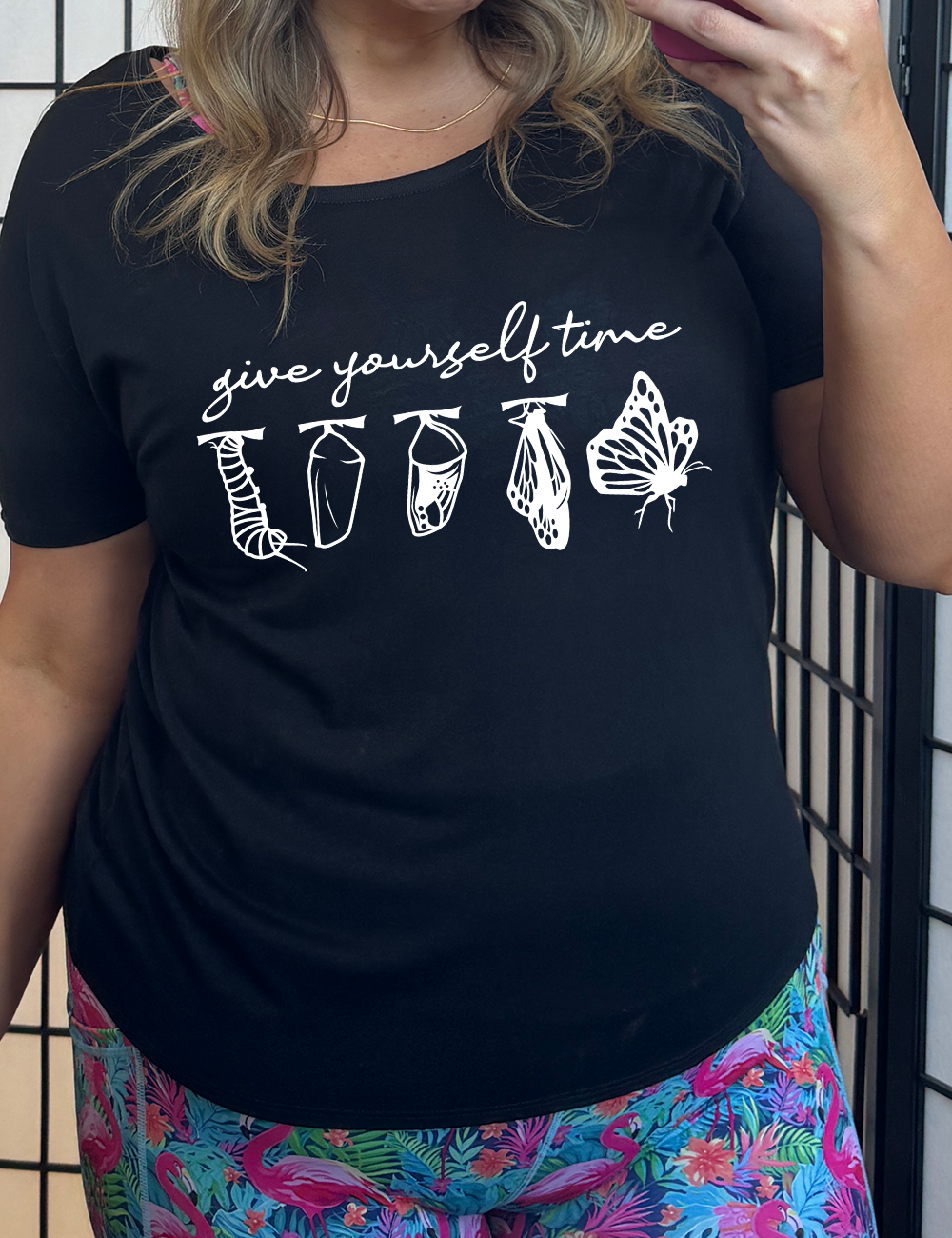 black slouchy tee with the graphic of the complete metamorphosis of a butterfly, with words above it saying "give yourself time"