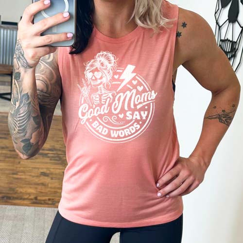 model wearing a peach muscle tank with the saying "good moms say bad words" and a female skeleton rock symbol hand and lightning bolt