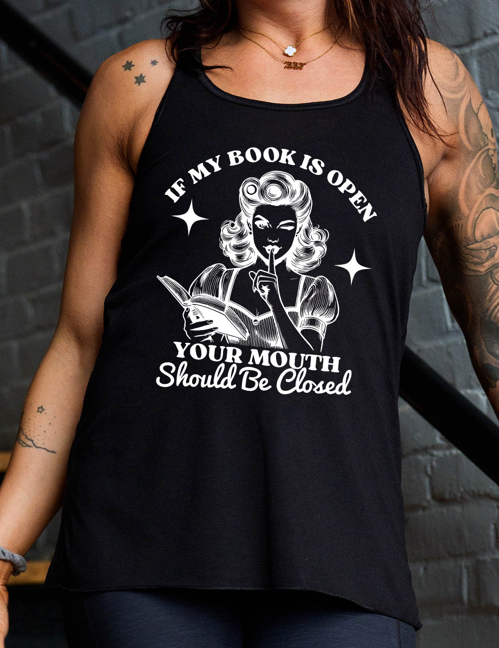 Black racerback flowy tank with the words "If my book is open your mouth should be closed" on it, around the graphic of 950s era woman, holding a finger to her lips, with an open book in her other hand, with a star on either side of her