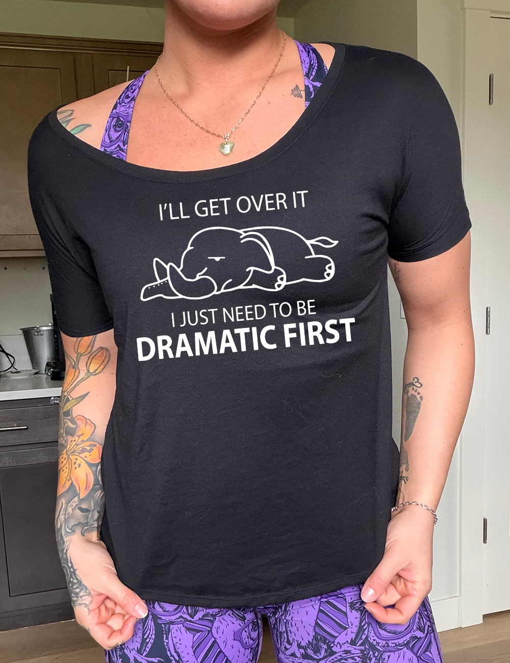black slouchy tee with the outlined graphic of an exhausted elephant flat on the floor, and the words around it saying "I'll get over it I just need to be dramatic first"