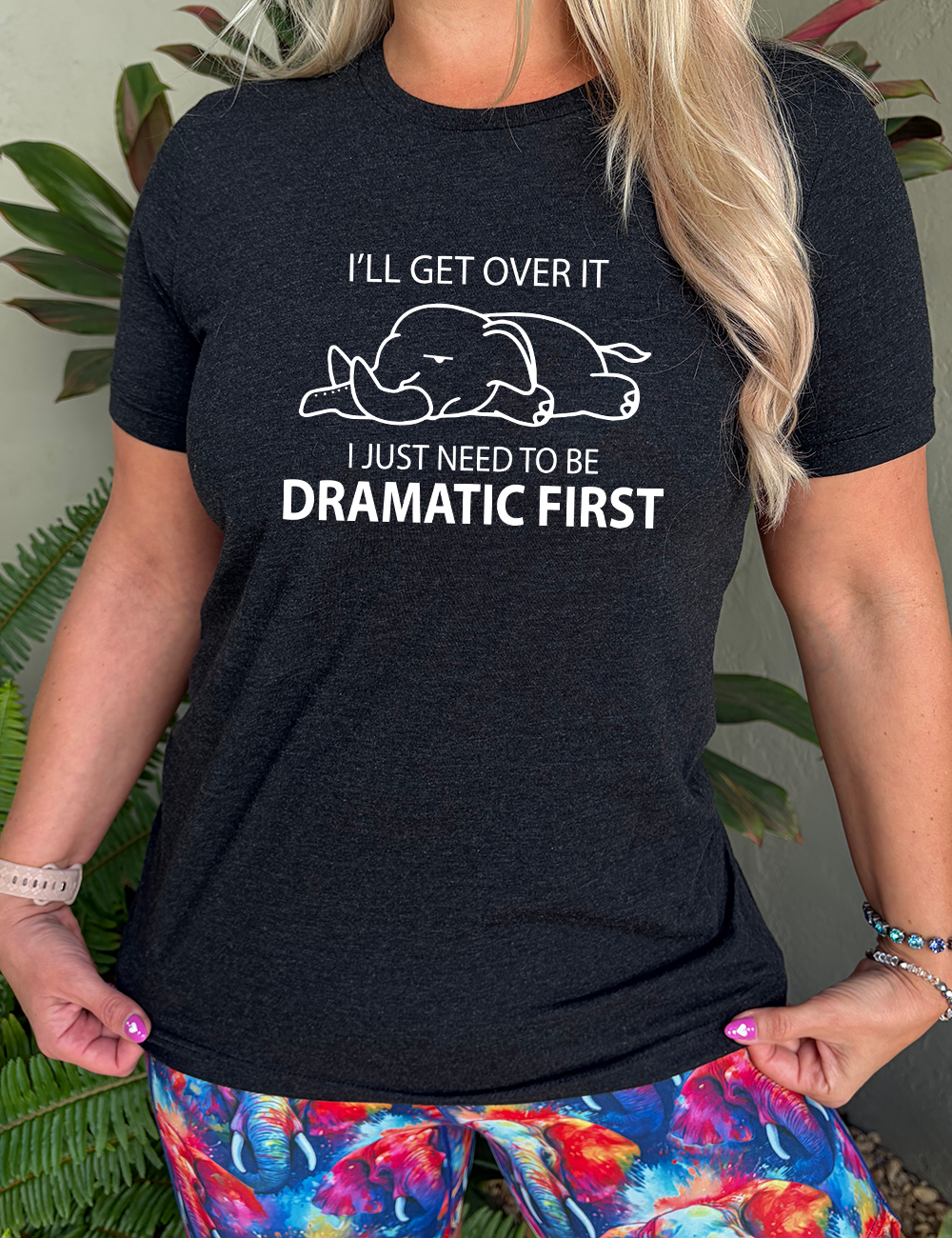 black unisex tee with the outlined graphic of an exhausted elephant flat on the floor, and the words around it saying "I'll get over it I just need to be dramatic first"