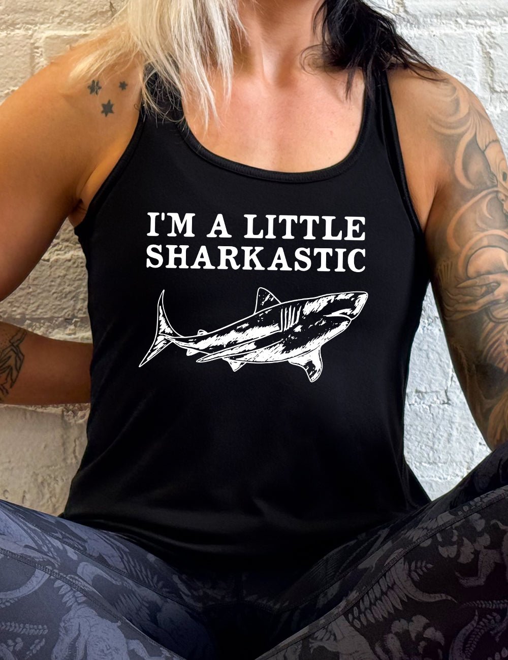 black racerback flowy tank with the words "I'm a little sharkastic" on it, over the graphic of a shark