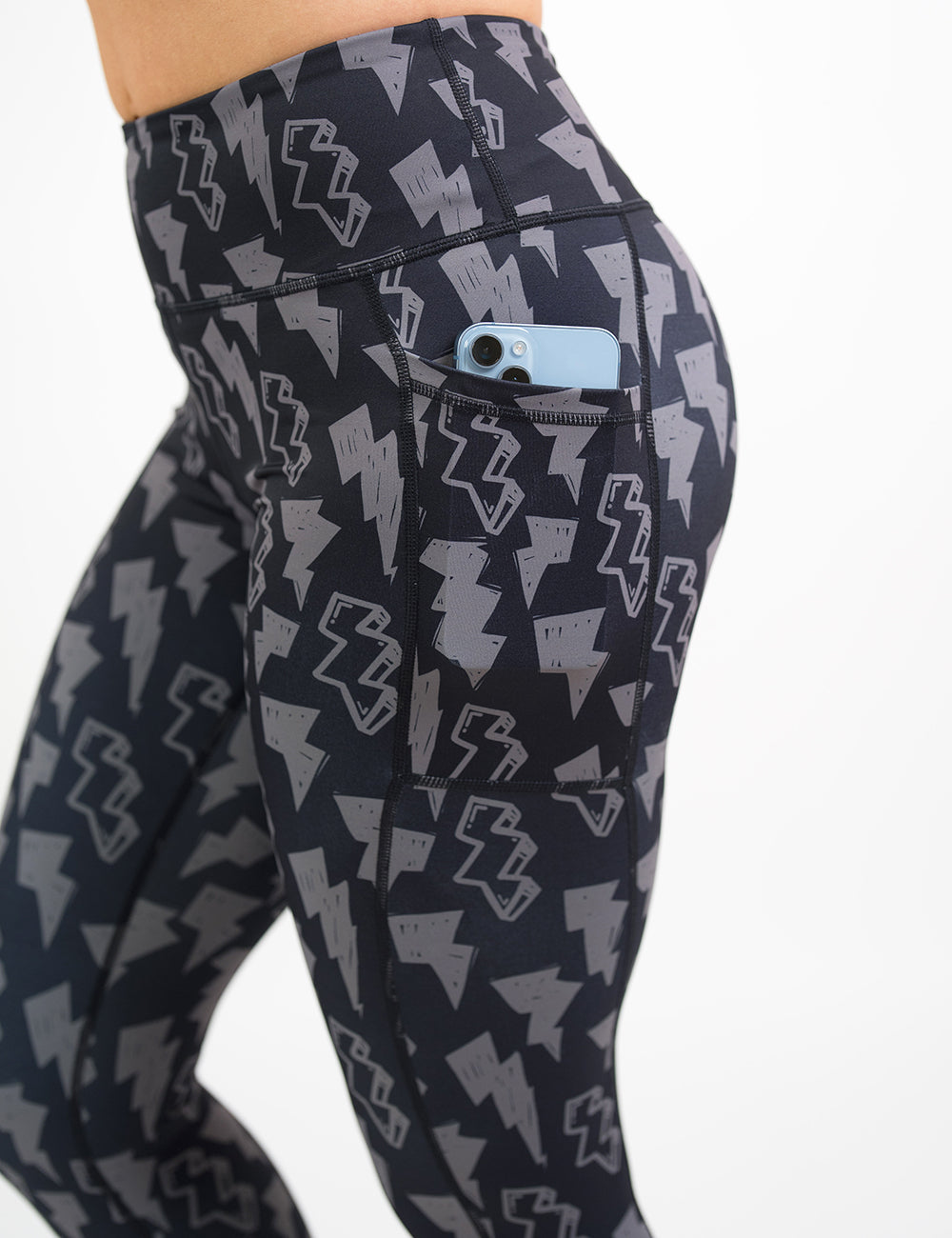 close up of the black leggings with grey thunder bolts holding a phone in its pocket