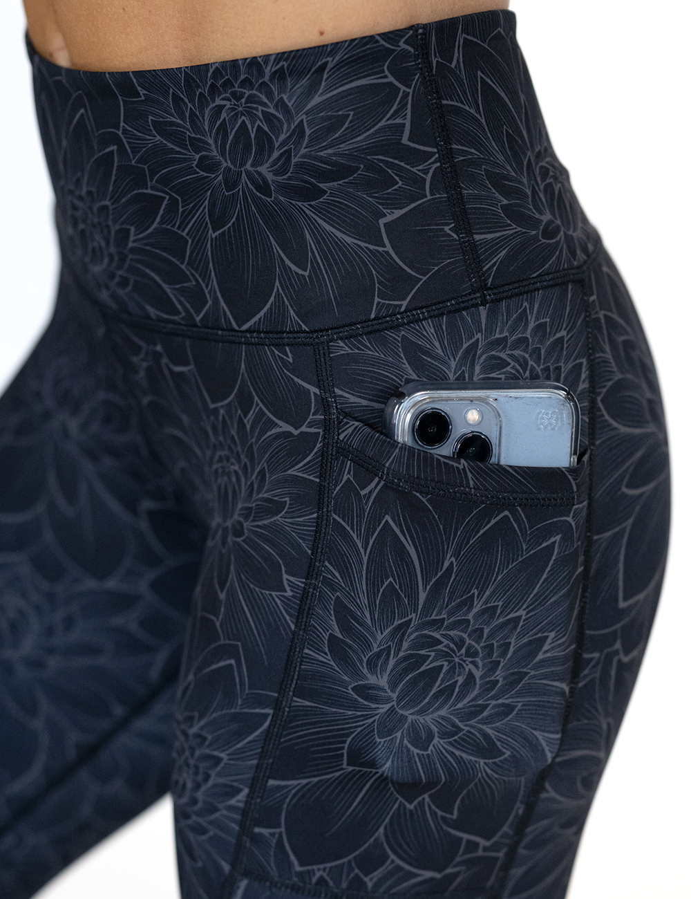 close up of the black lotus flower leggings pocket holding a phone against a white background
