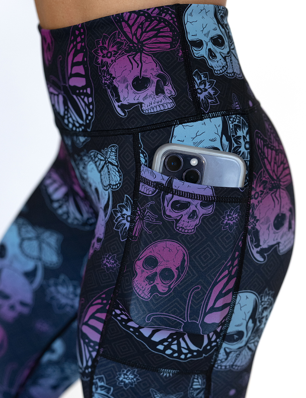 close up of the blue and purple skulls surrounded by butterflies leggings pocket holding a phone