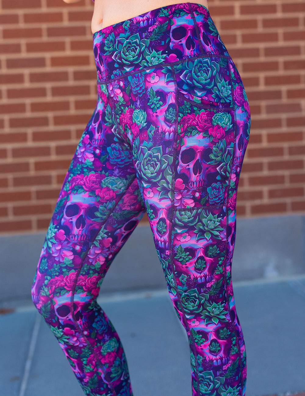 close up of the Floral and skull patterned leggings against a brick wall