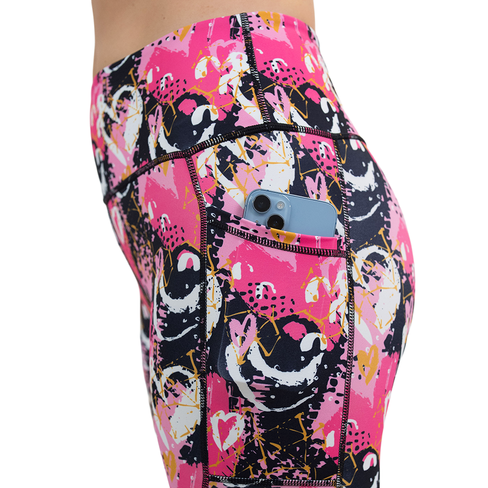 white hearts against a bold pink, black, and yellow pattern leggings with a phone in its pocket against a white background