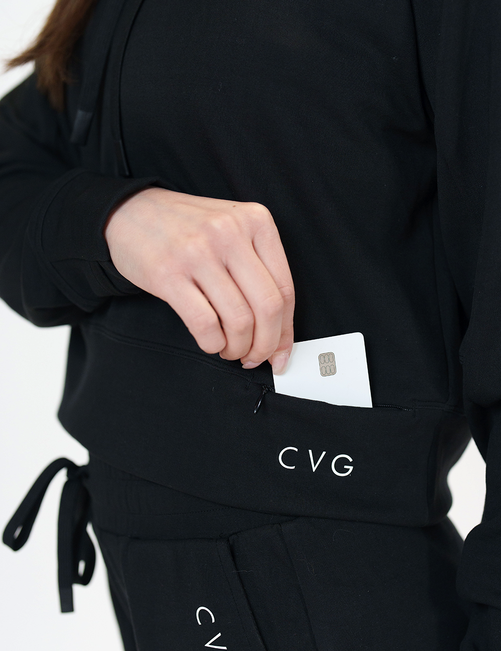 close up of the pocket of the black drawstring hoodie holding a credit card in the pocket against a white background
