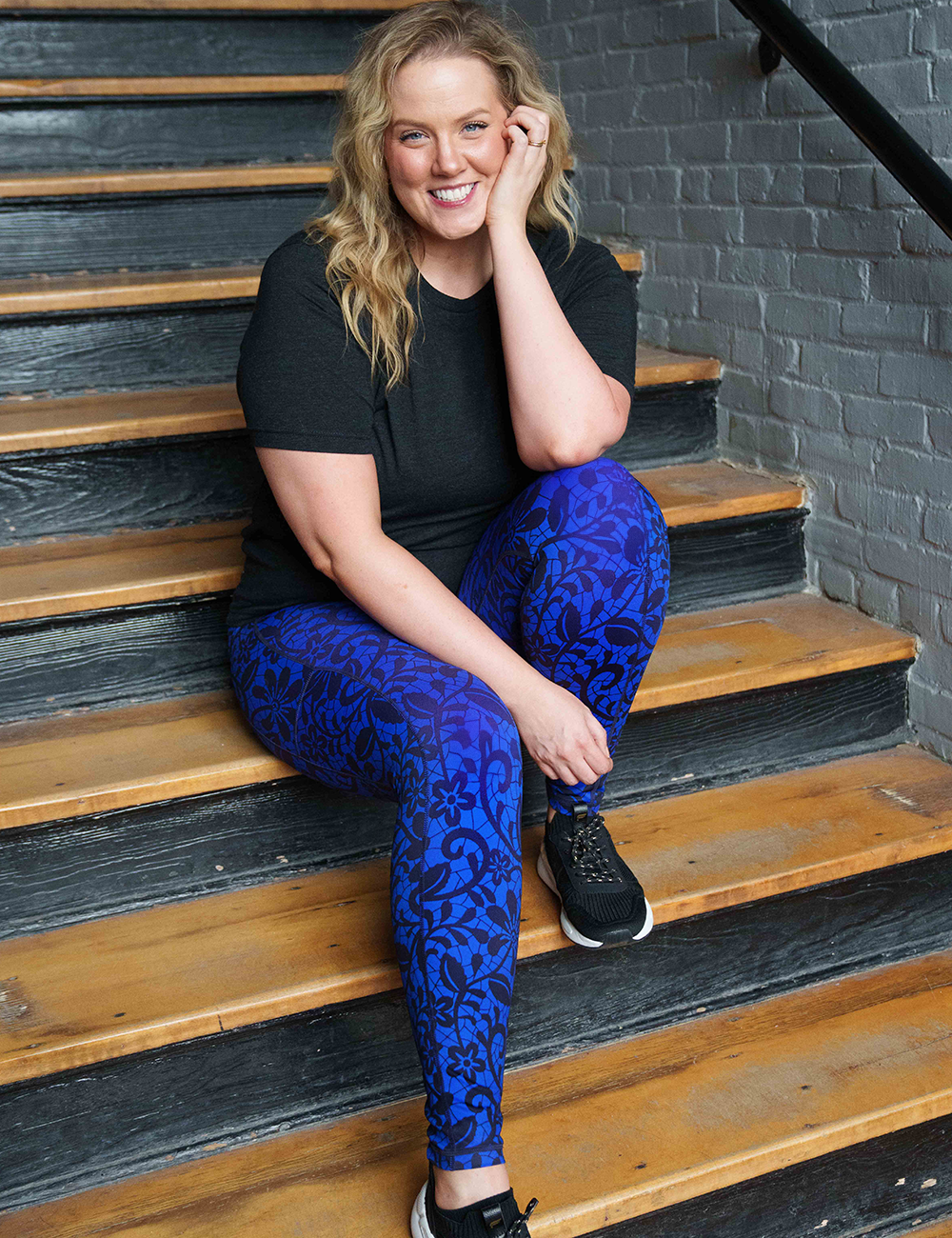 model wearing a black shirt with the full length midnight lace leggings while sitting on the stairs