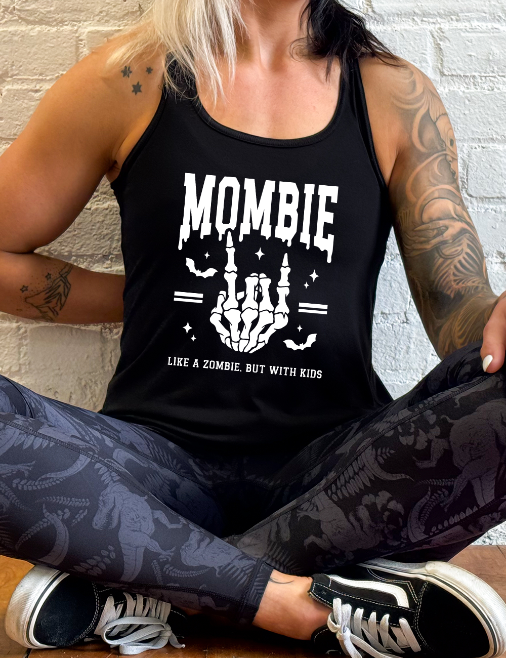 black racerback flowy tank with the big word "mombie" on it, with the graphic of a skeletal hand giving the rocker sign, with a couple bats and a number of little stars, and two equal signs, with small words underneath it all saying "like a zombie, but with kids"