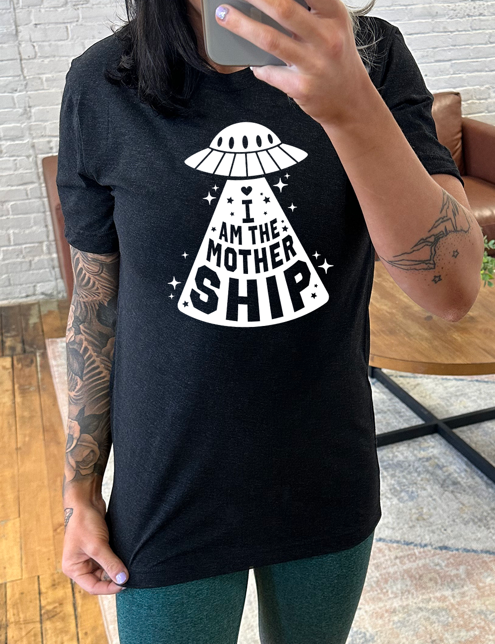 black unisex tee with the words "I am the mothership" on it within the beam of a UFO, with a heart above the words, and a number of stars scattered around