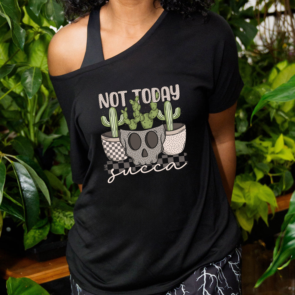 A person wearing a black slouchy tee with 'NOT TODAY SUCCA' text and a graphic of a skull, cacti, and succulent plant on it, standing in a garden setting.
