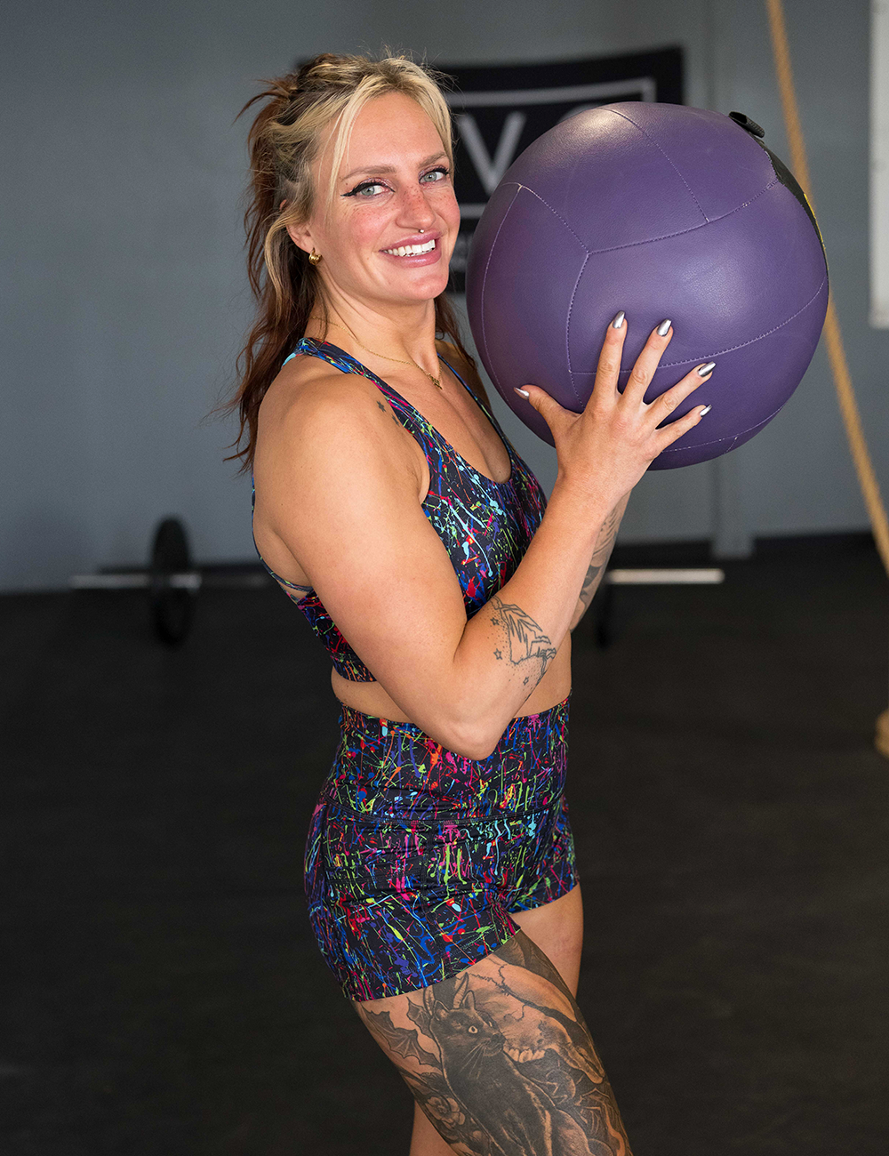 model wearing the rainbow paint splatter shorts in the gym holding a medicine ball