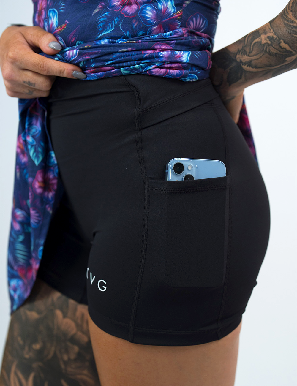 tropical flower themed active dress rolled up to show the built in shorts underneath with a phone in the pocket against a white background