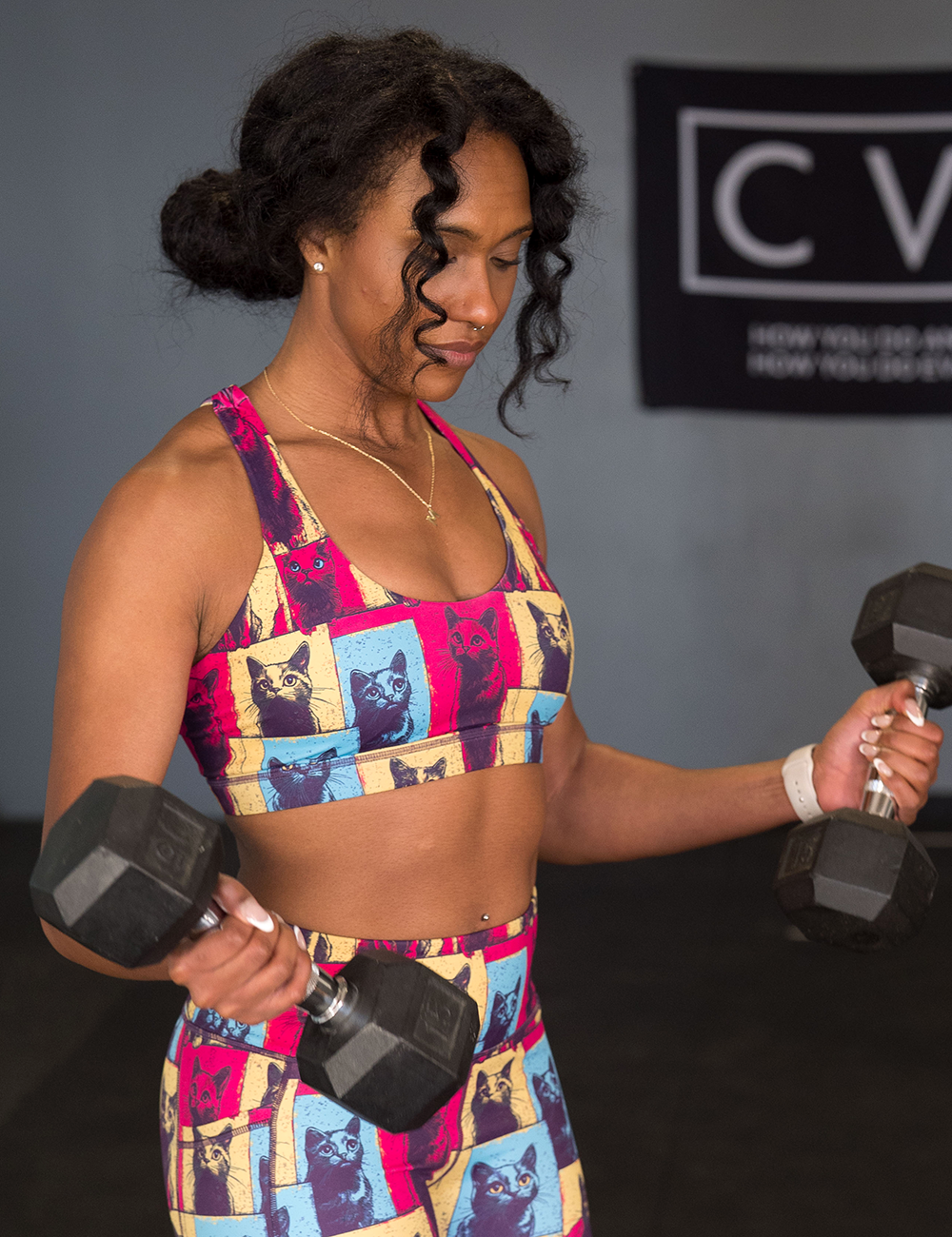 model wearing the red, blue, and yellow patchwork cat print bra and leggings working out in the gym