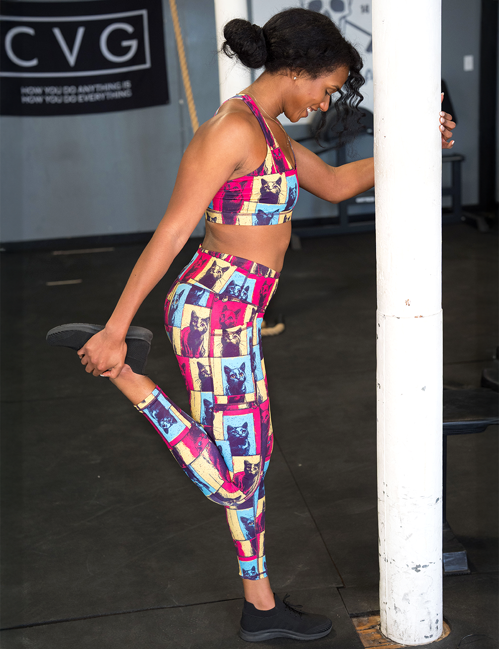 model wearing the red, yellow, and blue cat leggings and sports bra stretching in the gym