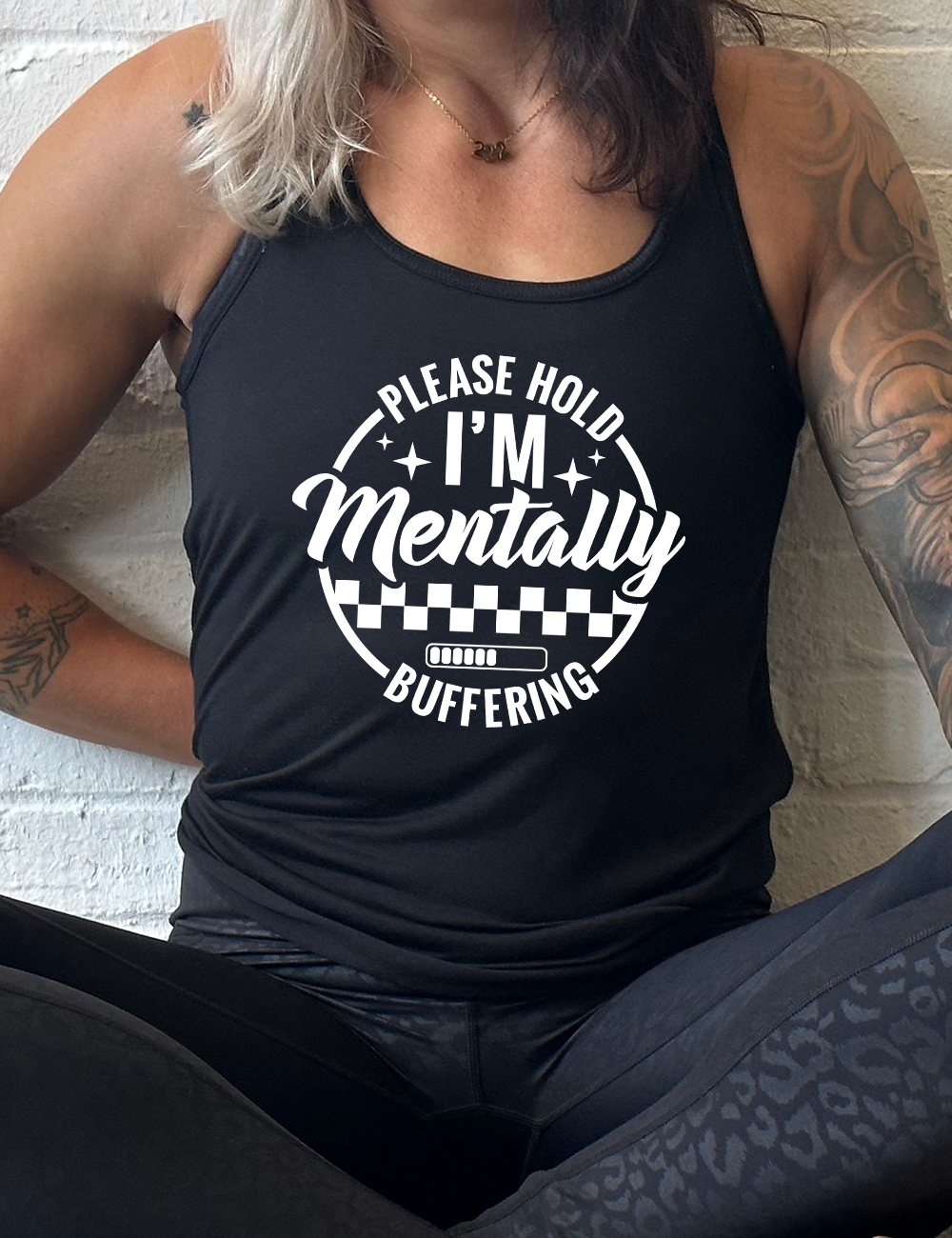 black racerback flowy tank with the words "please hold I'm mentally buffering" written on it in a circle graphic, with some of the words part of the arches, and within the circle there are two layers of checkerboard as well as a buffering bar, which is about 6 out of 10 full