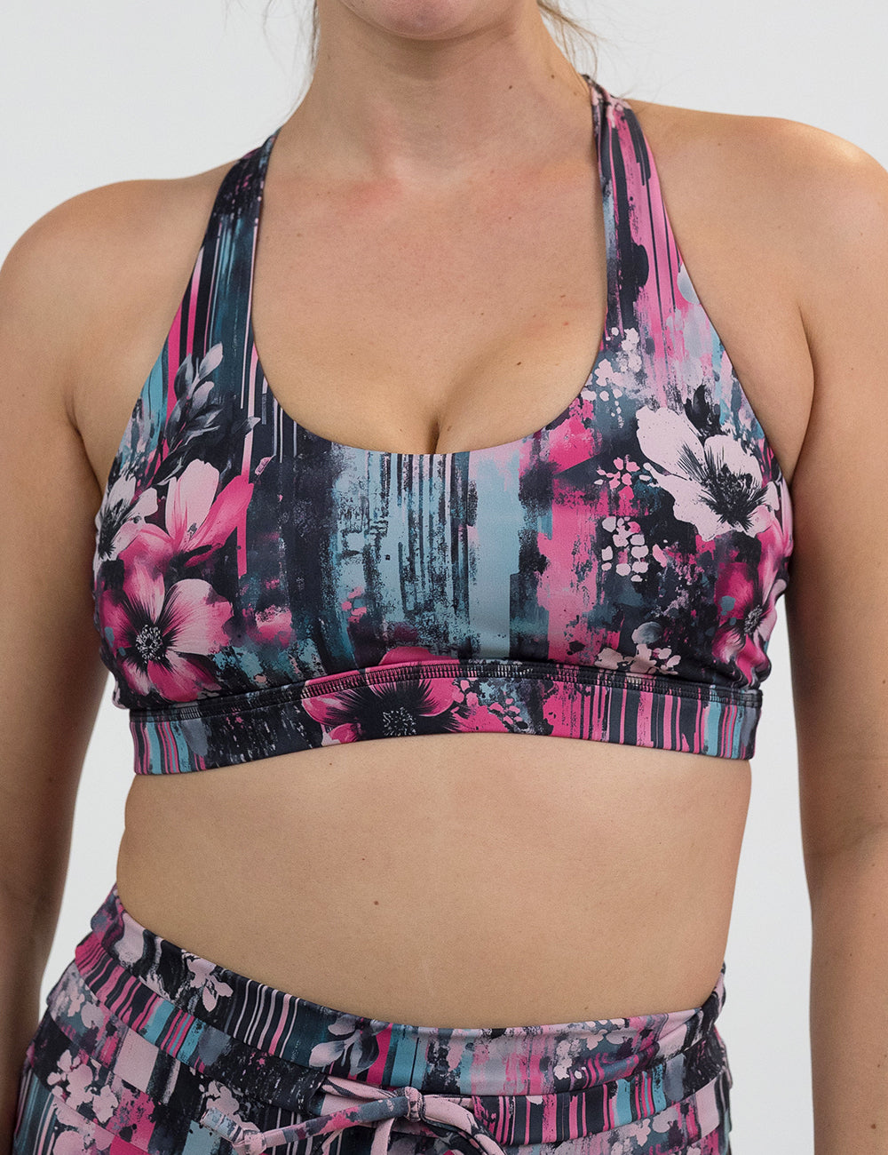 front of the pink flowers against a bold teal and pink striped background pattern butterfly back bra against a white background