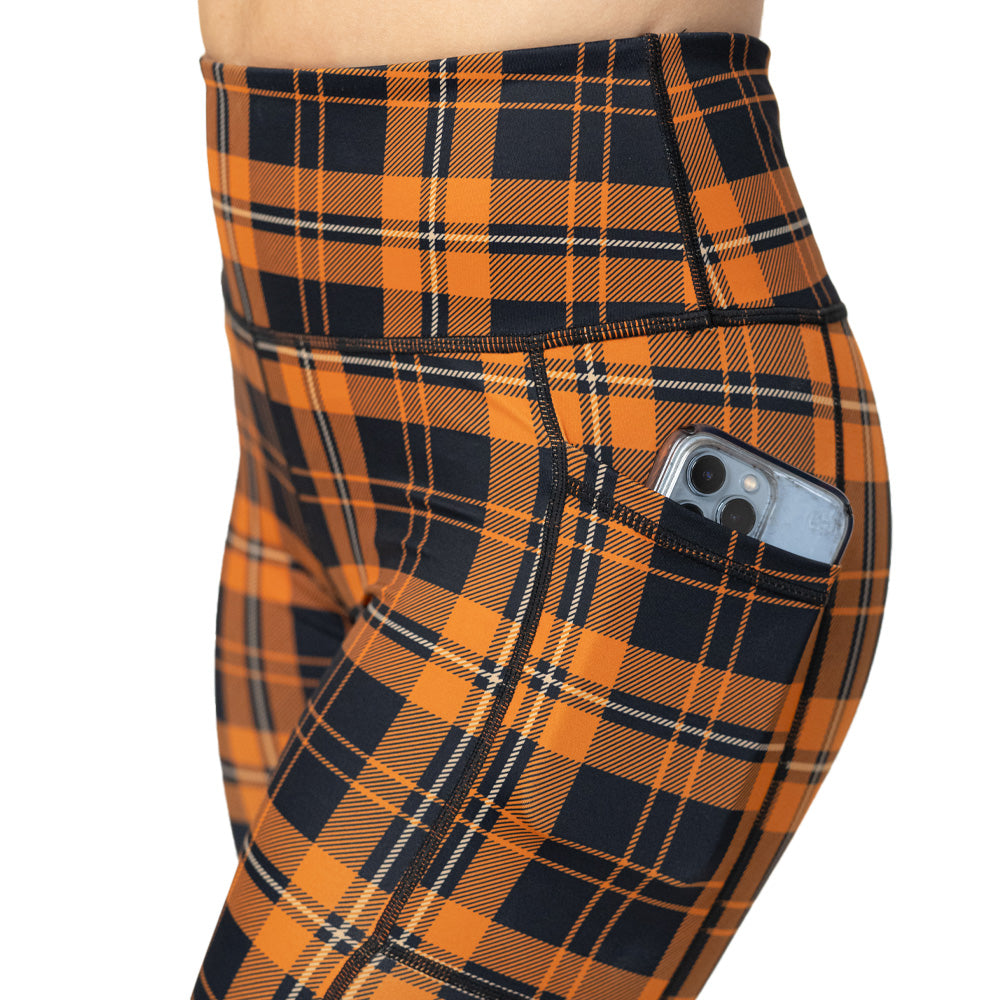 Orange and black plaid leggings with a phone in the pocket on a white background