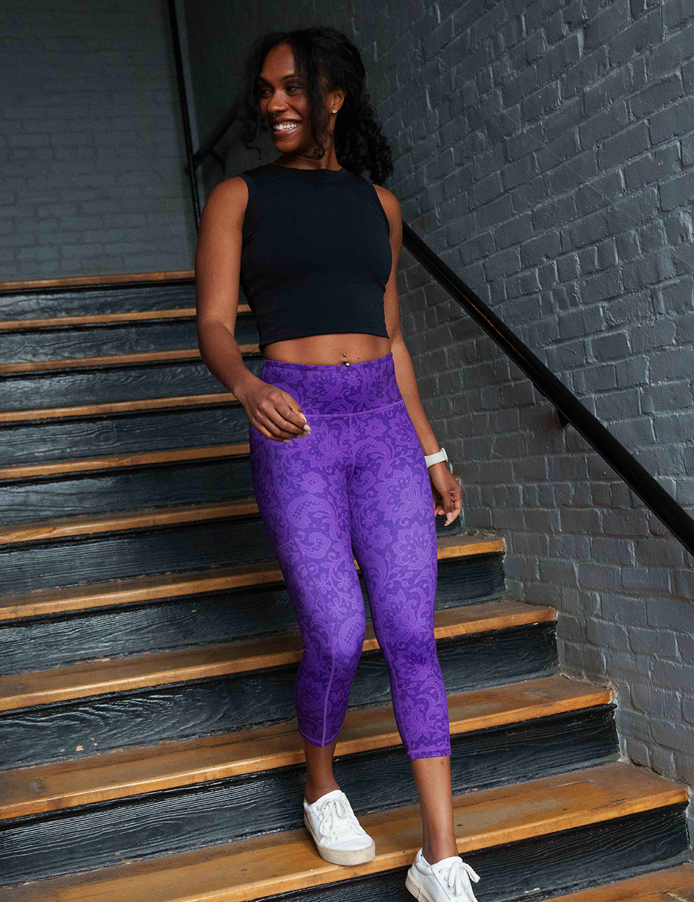 model wearing a black shirt with the purple lace capri leggings going down the stairs