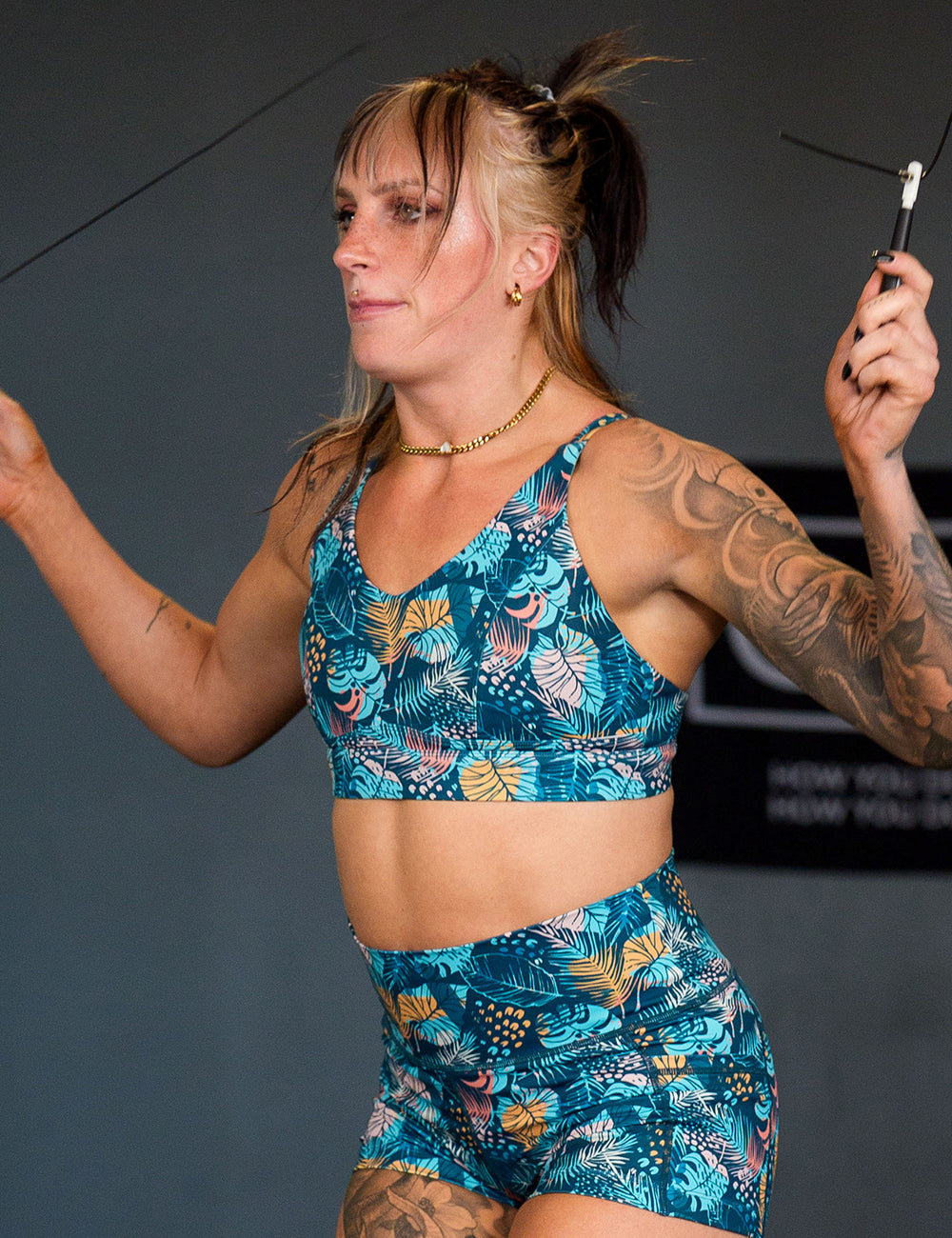 model wearing the blue, yellow, pink, and red tropical leaves print vitality bra doing jump rope in the gym