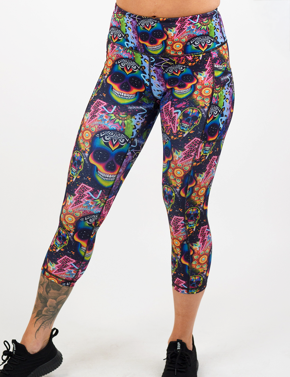 brightly colored psychedelic skulls pattern against a busy background full of designs capri leggings facing the front against a white background