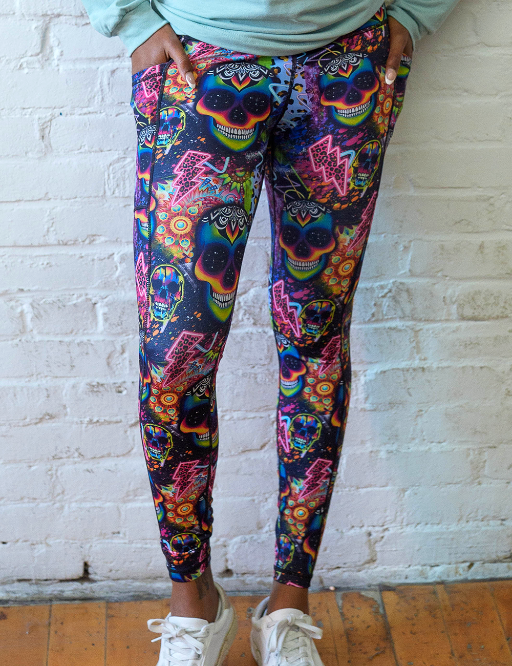 brightly colored psychedelic skulls pattern against a busy background full of designs full length leggings facing the front against a white brick background