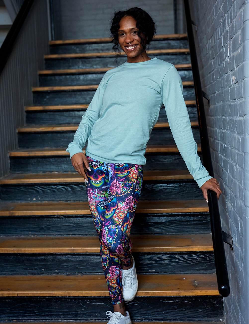 model wearing the brightly colored psychedelic skulls pattern against a busy background full of designs full length leggings against a rustic staircase background