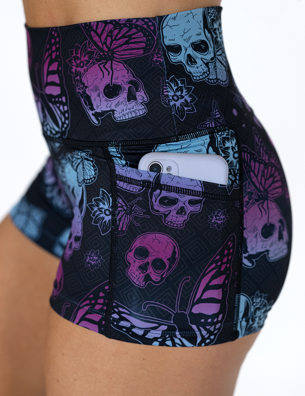close up of the blue and purple skulls surrounded by butterflies shorts pocket holding a phone