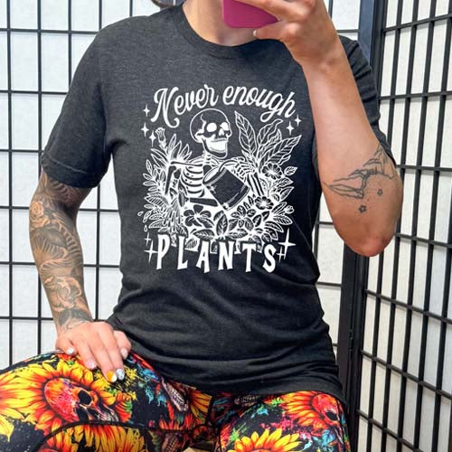 model wearing the black unisex shirt with the saying "Never Enough Plants" and skeleton graphic on it in white