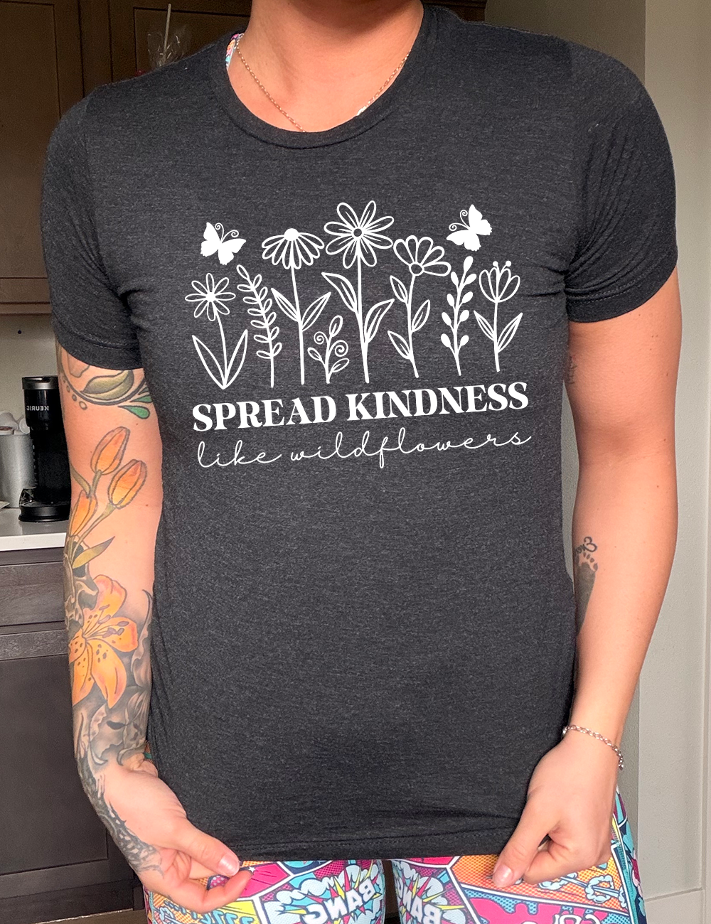 black unisex tee with the graphics of wildflowers in a row, with the words "spread kindness like wildflowers" written underneath