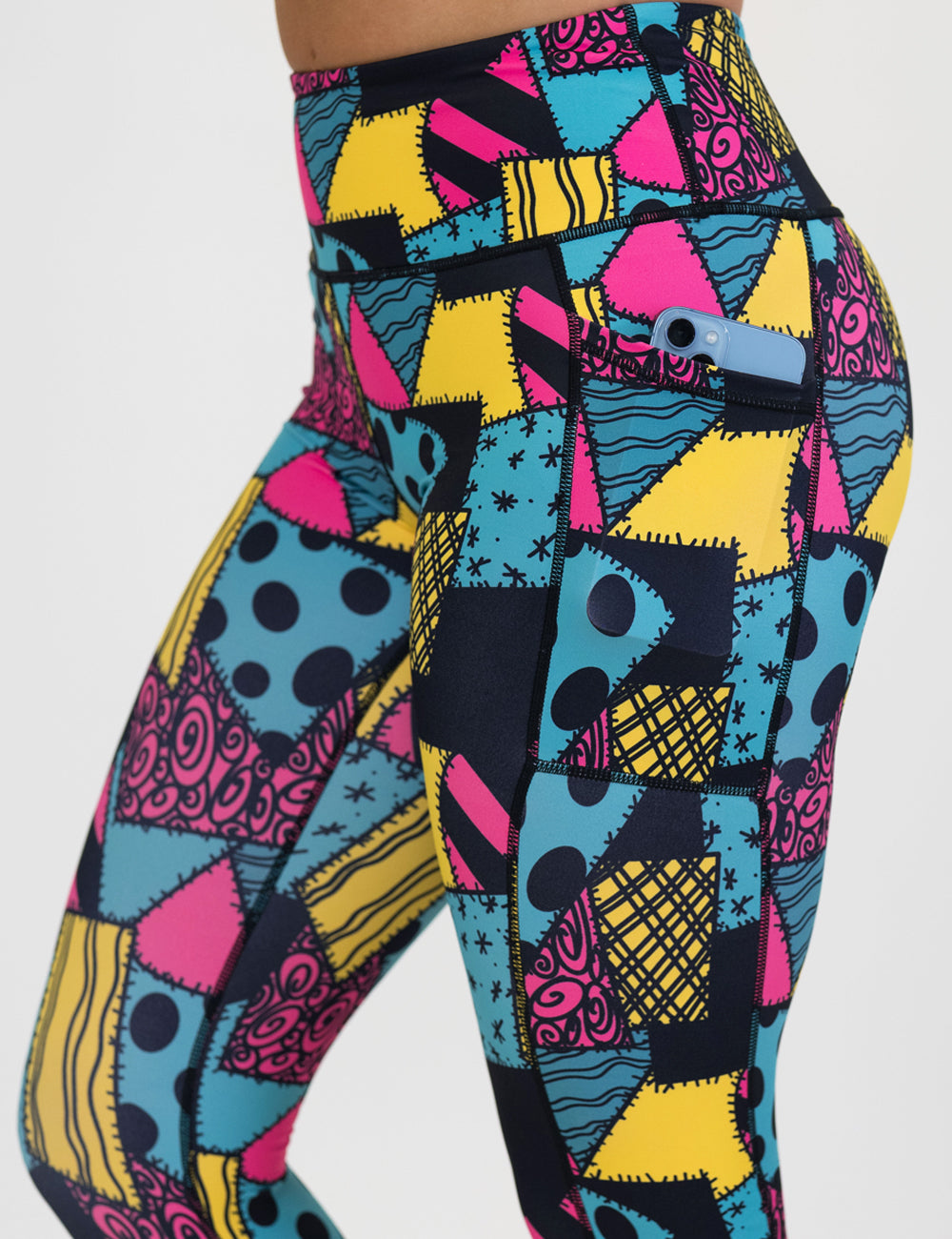 close up of the yellow, teal, and pink patchwork design leggings with a phone in its pocket