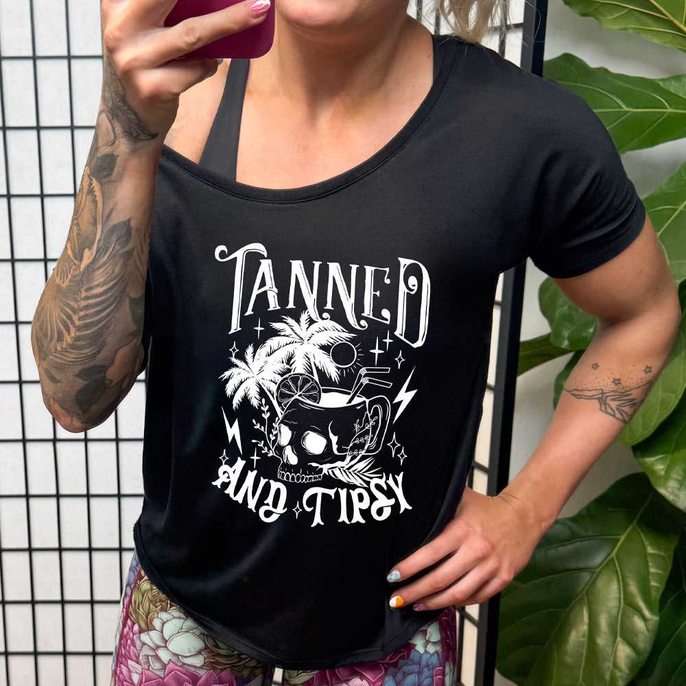 shirt with a drink inside a skull cup graphic on it that says "Tanned and Tipsy"